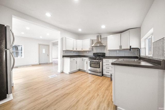 kitchen with wall chimney exhaust hood, light wood-style flooring, appliances with stainless steel finishes, a sink, and backsplash