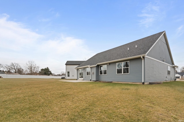 rear view of property with a shingled roof, a patio area, and a yard