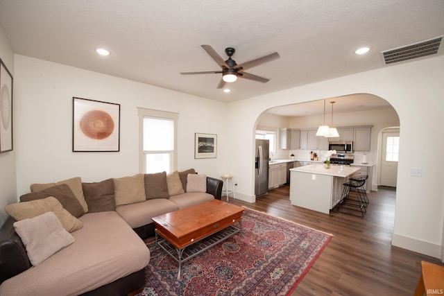 living area with arched walkways, dark wood-style floors, visible vents, and recessed lighting