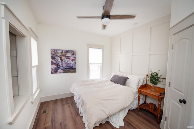 bedroom with a decorative wall, wood finished floors, a ceiling fan, baseboards, and visible vents