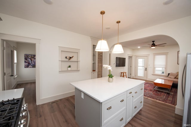 kitchen featuring arched walkways, dark wood-style flooring, a kitchen island, light countertops, and appliances with stainless steel finishes