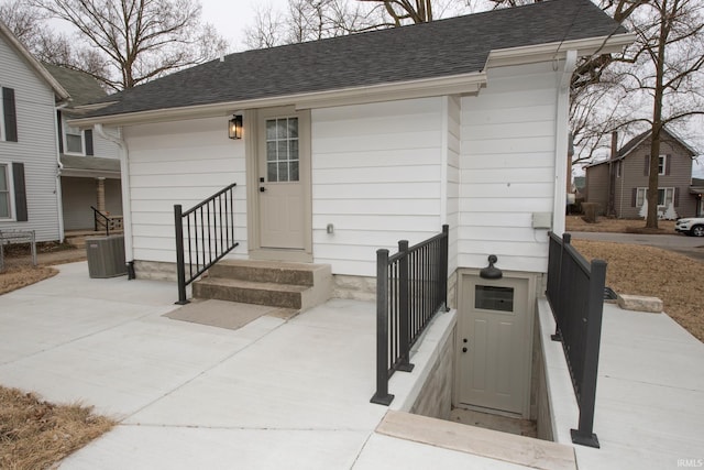 entrance to property with central AC and a shingled roof