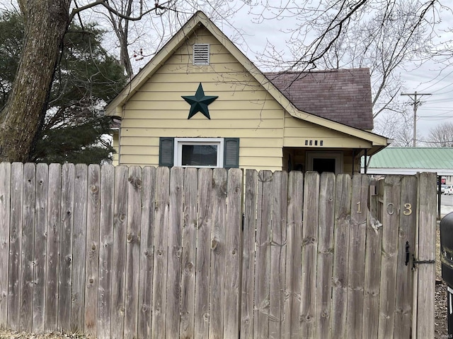 view of side of property with roof with shingles and fence