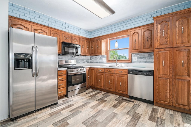 kitchen featuring brown cabinets, light wood finished floors, light countertops, appliances with stainless steel finishes, and a sink