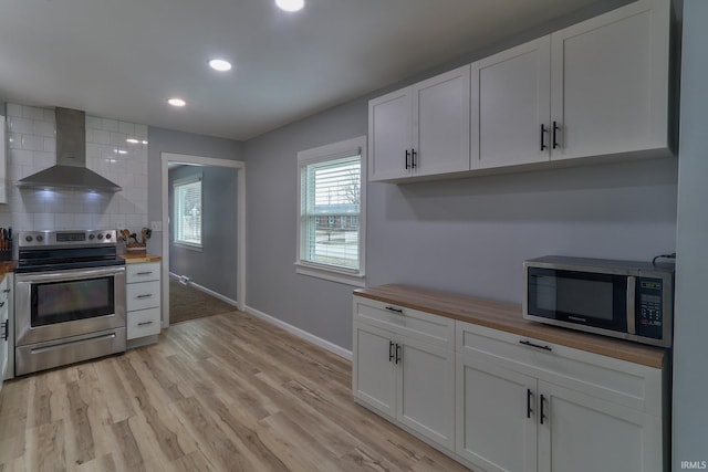 kitchen with light wood finished floors, butcher block counters, decorative backsplash, appliances with stainless steel finishes, and wall chimney range hood