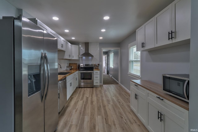 kitchen with light wood-style flooring, stainless steel appliances, a sink, white cabinets, and wall chimney exhaust hood