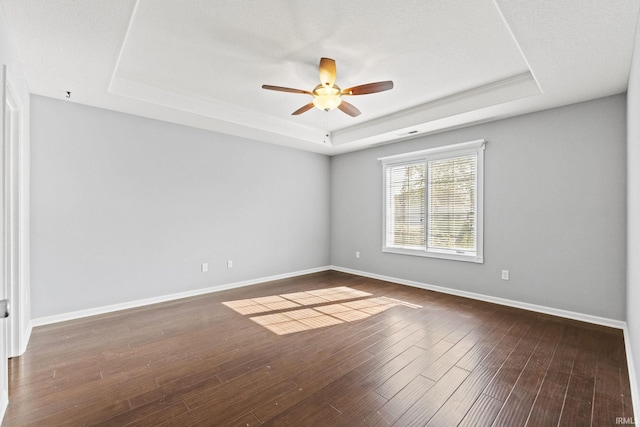 spare room with ceiling fan, wood finished floors, a raised ceiling, and baseboards