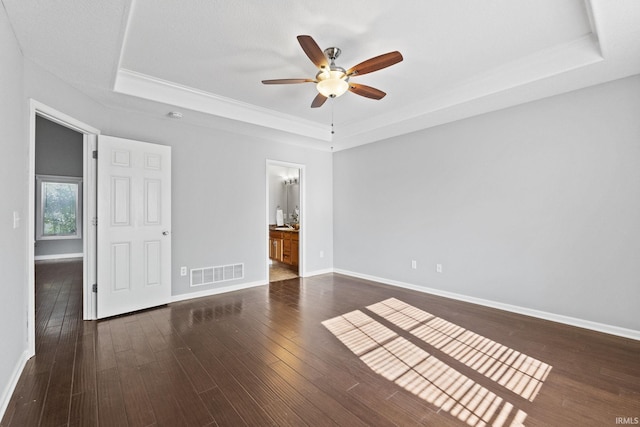 unfurnished bedroom featuring baseboards, visible vents, a raised ceiling, and dark wood finished floors