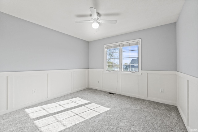 carpeted spare room with a decorative wall, wainscoting, visible vents, and a ceiling fan