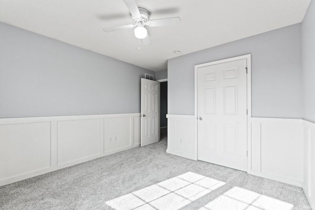 unfurnished bedroom with a wainscoted wall, ceiling fan, carpet flooring, and a decorative wall