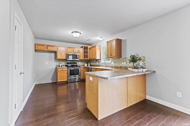 kitchen featuring stainless steel appliances, a peninsula, decorative backsplash, dark wood finished floors, and glass insert cabinets