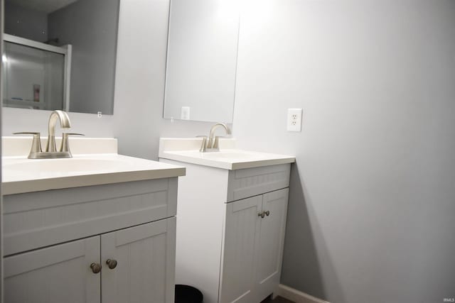 bathroom with a sink, a stall shower, two vanities, and baseboards