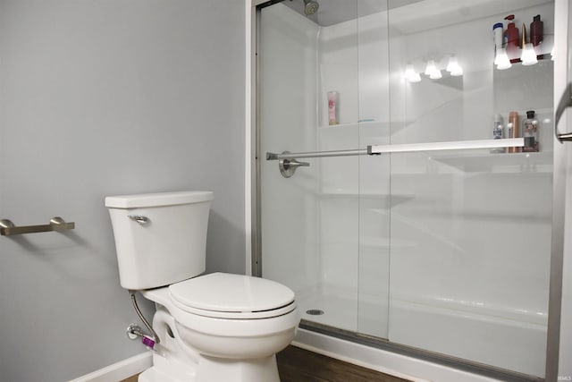 full bath featuring toilet, a shower stall, baseboards, and wood finished floors