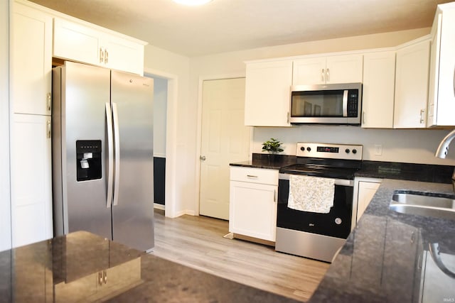 kitchen with stainless steel appliances, white cabinetry, a sink, and light wood finished floors