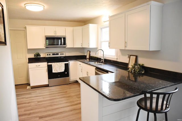 kitchen with light wood-style flooring, stainless steel appliances, a peninsula, a sink, and white cabinets