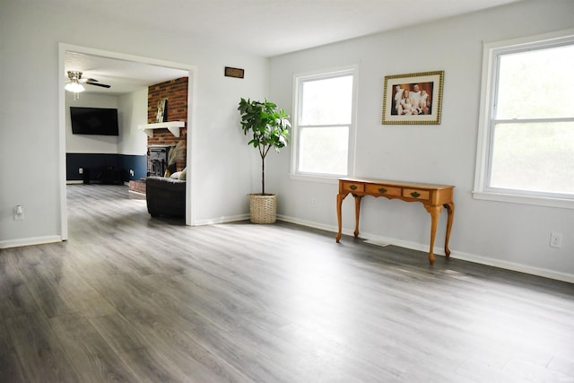 empty room with a large fireplace, ceiling fan, baseboards, and wood finished floors