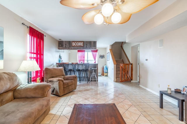 living room featuring light tile patterned floors, baseboards, ceiling fan, stairway, and a bar