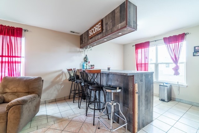 kitchen with a peninsula, visible vents, a kitchen breakfast bar, baseboards, and tile patterned floors