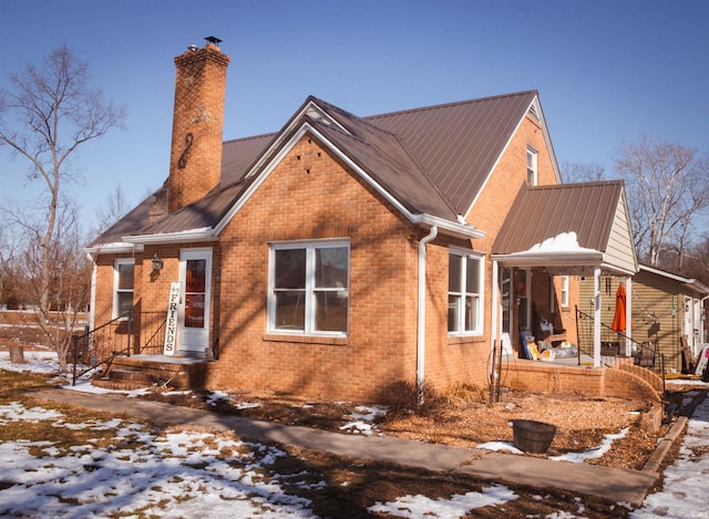 view of snow covered exterior featuring metal roof, brick siding, and a chimney