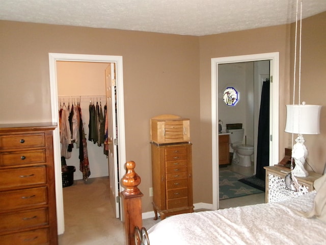 bedroom with a walk in closet, a closet, ensuite bathroom, light carpet, and a textured ceiling