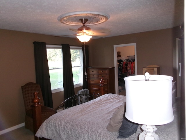 bedroom with a closet, a spacious closet, a ceiling fan, a textured ceiling, and baseboards