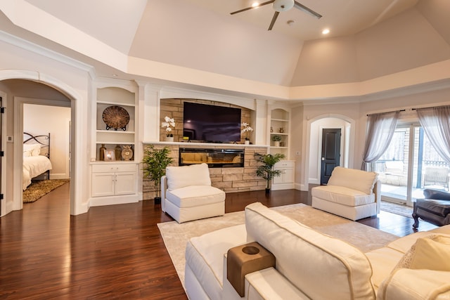 living area with arched walkways, ceiling fan, dark wood-style flooring, built in shelves, and high vaulted ceiling