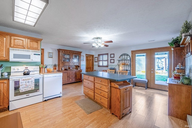 kitchen featuring a textured ceiling, white appliances, a kitchen island, light wood finished floors, and dark countertops