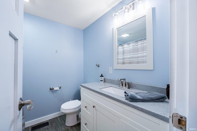 bathroom featuring visible vents, toilet, vanity, wood finished floors, and baseboards