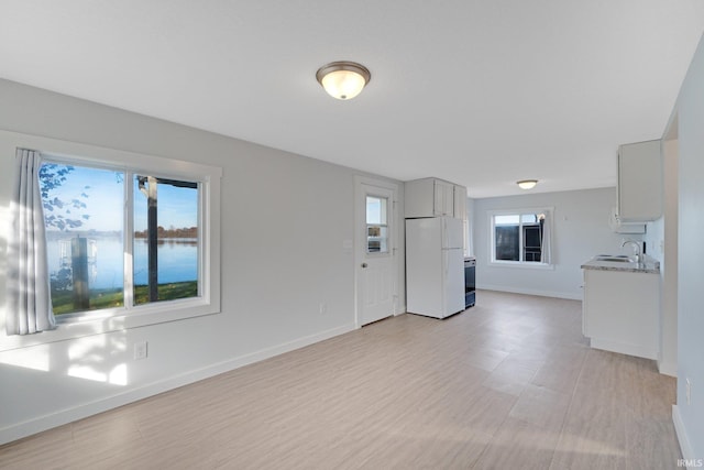 unfurnished living room featuring a water view, light wood-type flooring, baseboards, and a sink