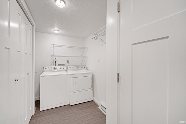 clothes washing area with a baseboard radiator, washing machine and dryer, a textured ceiling, wood finished floors, and laundry area