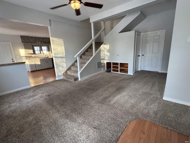 unfurnished living room with visible vents, a ceiling fan, carpet flooring, baseboards, and stairs