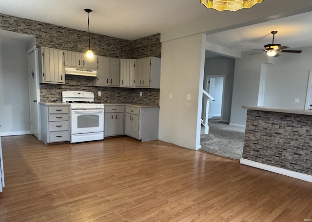 kitchen with white gas range, light countertops, backsplash, light wood-type flooring, and under cabinet range hood