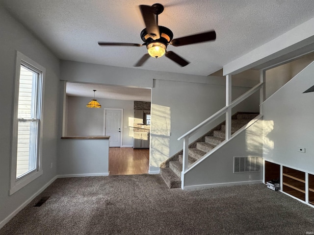 empty room featuring a wealth of natural light, visible vents, stairway, and carpet flooring