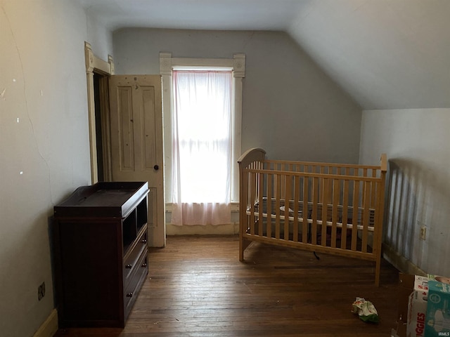 bedroom featuring a crib, wood-type flooring, and vaulted ceiling