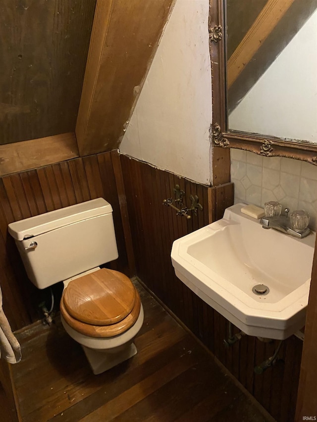 half bath with toilet, wooden walls, wood finished floors, a sink, and tasteful backsplash