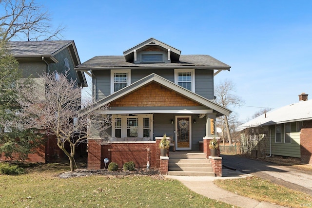 american foursquare style home with covered porch, a front yard, a ceiling fan, and brick siding