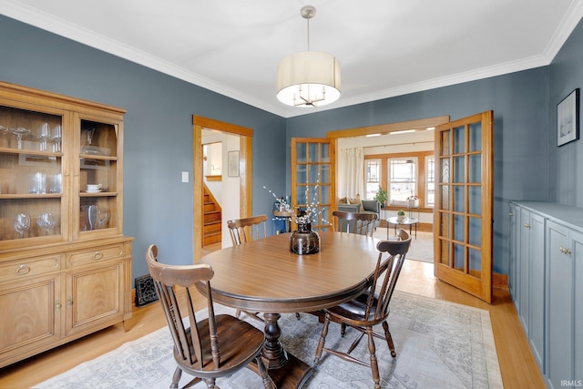 dining space featuring french doors, light wood finished floors, ornamental molding, baseboards, and stairs