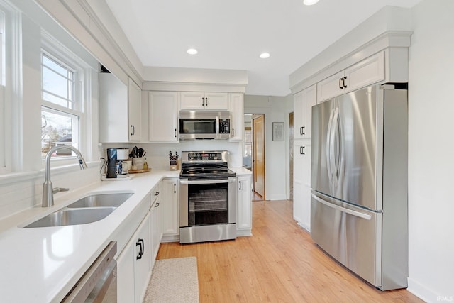 kitchen featuring white cabinets, stainless steel appliances, light countertops, light wood-style floors, and a sink