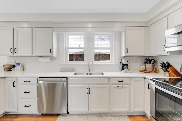 kitchen featuring light countertops, backsplash, appliances with stainless steel finishes, white cabinets, and a sink