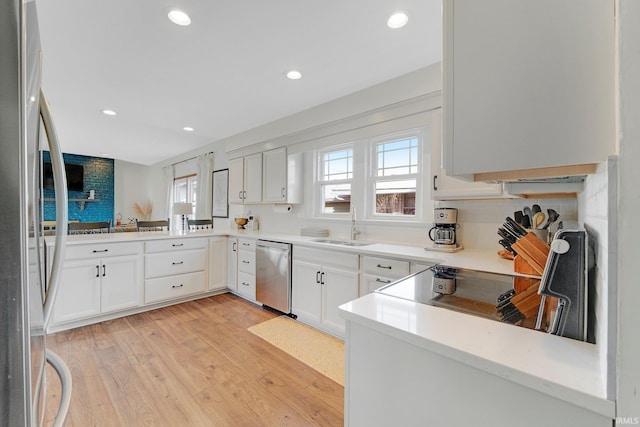 kitchen featuring stainless steel appliances, light wood finished floors, a sink, and white cabinets