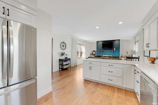 kitchen with white cabinets, light wood-style flooring, a peninsula, stainless steel appliances, and light countertops