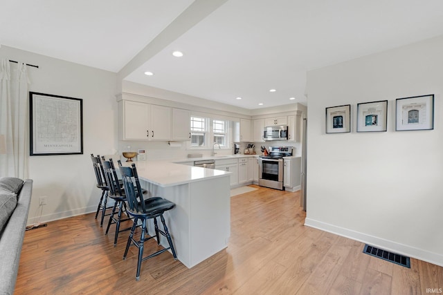 kitchen featuring stainless steel appliances, a peninsula, a sink, visible vents, and a kitchen breakfast bar