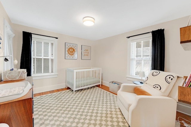 bedroom with a sink, a nursery area, baseboards, and wood finished floors