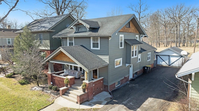 craftsman-style home with an outbuilding, driveway, a shingled roof, and a porch