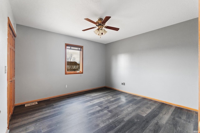 empty room with dark wood-style flooring, visible vents, ceiling fan, and baseboards