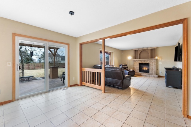 living area with a tiled fireplace, light tile patterned flooring, plenty of natural light, and baseboards