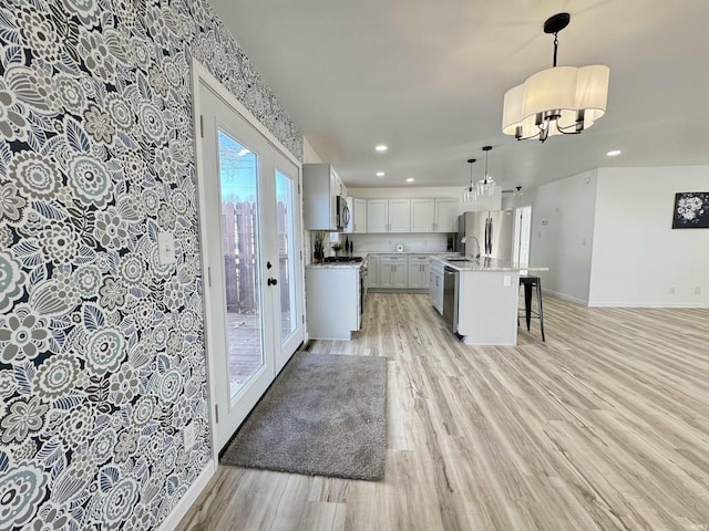 kitchen with baseboards, light wood-style flooring, stainless steel appliances, a kitchen bar, and pendant lighting