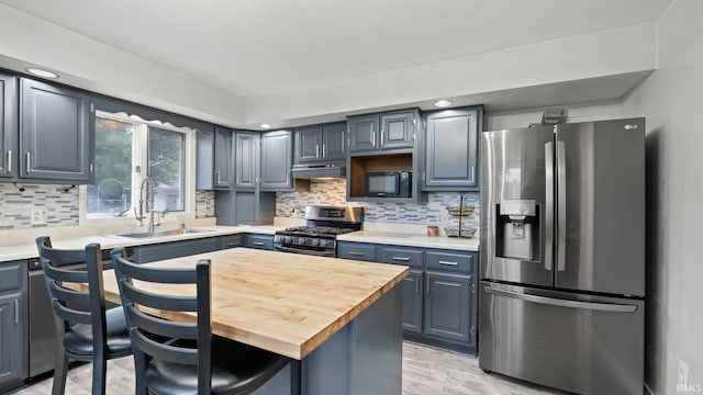 kitchen with light wood-style flooring, under cabinet range hood, stainless steel appliances, a sink, and tasteful backsplash