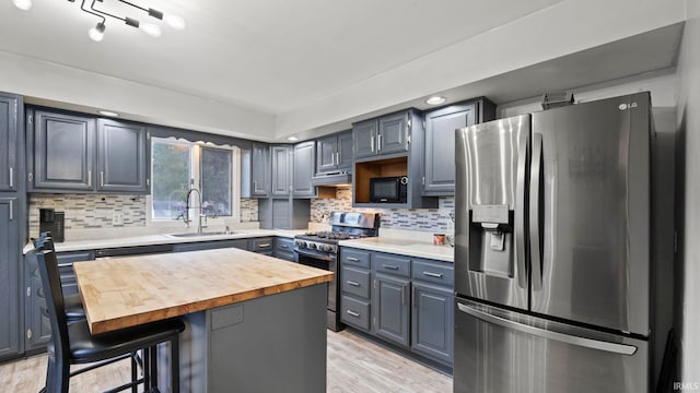 kitchen featuring stainless steel appliances, butcher block counters, backsplash, a sink, and a kitchen breakfast bar