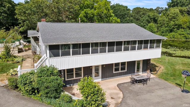 view of front of home featuring a shingled roof, a sunroom, a chimney, stairs, and a patio area